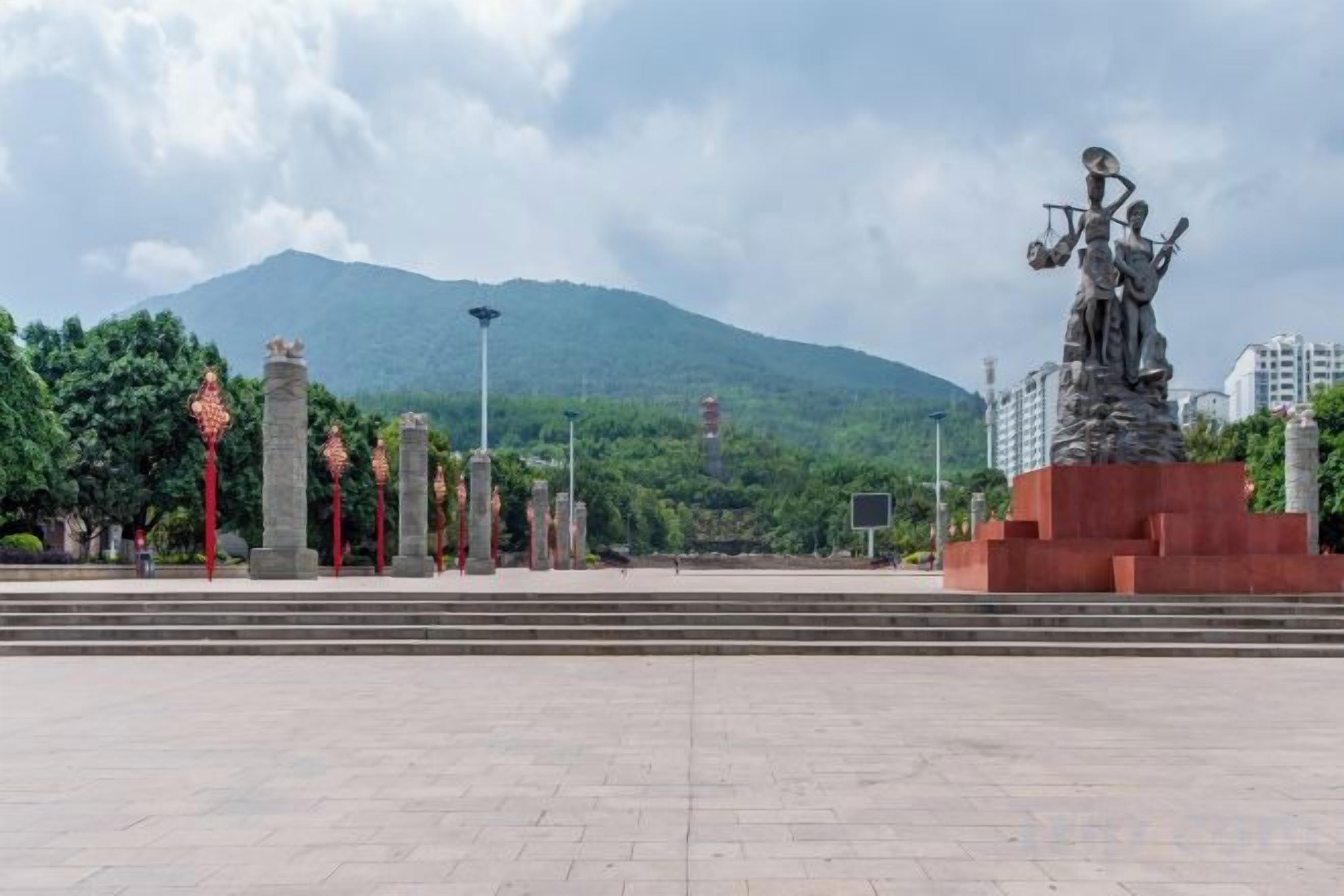 Una plaza con una estatua, escalones y una montaña al fondo.