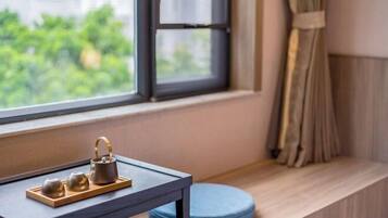 Una ventana con vistas a la vegetación, una mesita con un juego de té y un cojín azul sobre un repisa de madera.