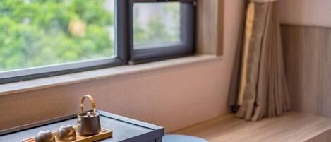Una ventana con vistas a la vegetación, una mesita con un juego de té y un cojín azul sobre un repisa de madera.