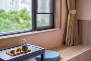 A window with a view of greenery, a small table with a tea set, and a blue cushion on a wooden ledge. - Manya Hotel (Xinping)