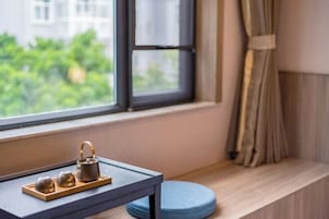 Una ventana con vistas a la vegetación, una mesita con un juego de té y un cojín azul sobre un repisa de madera.