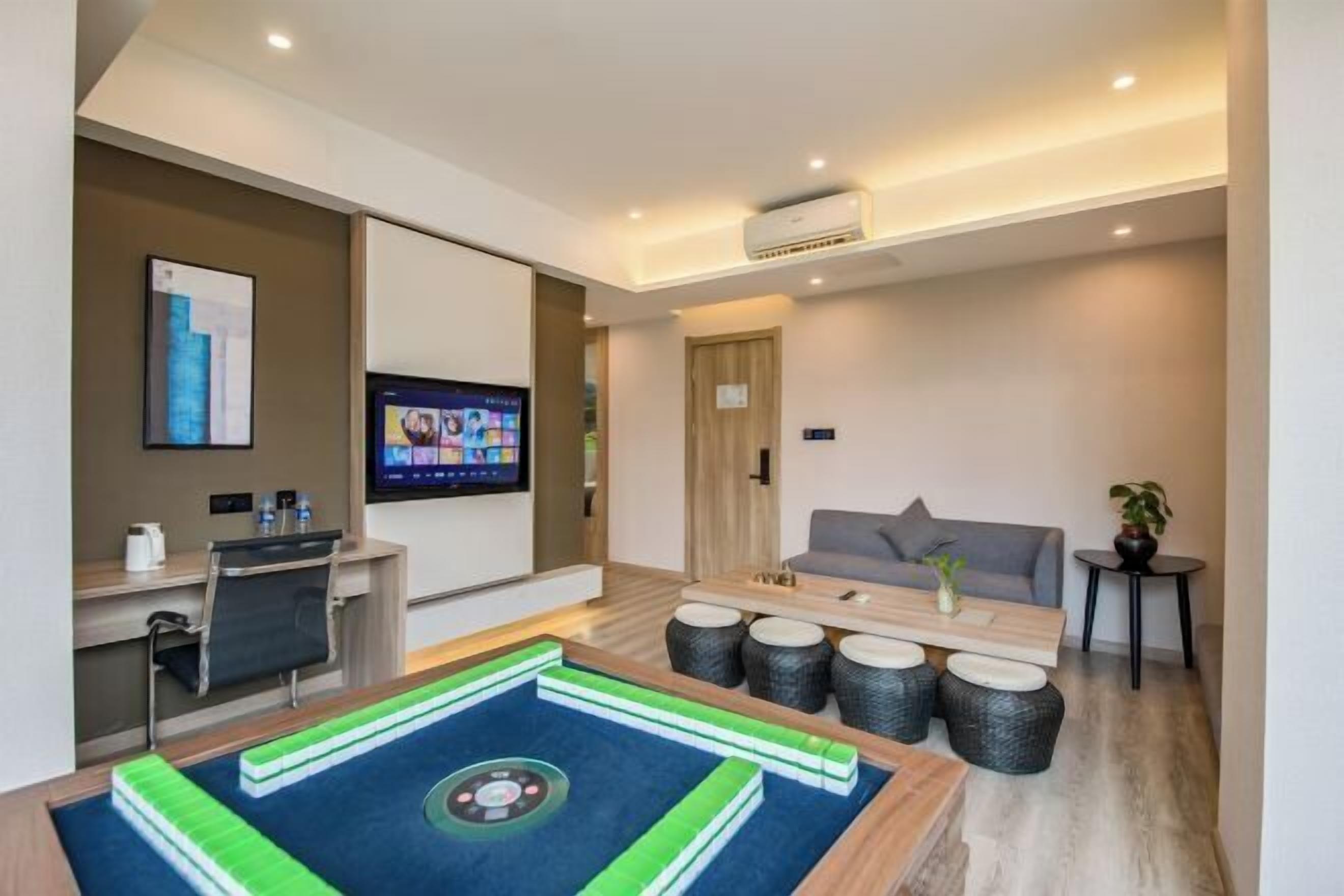 A modern hotel room with a flat-screen TV, a massage table, a sofa, and a small table with a plant.