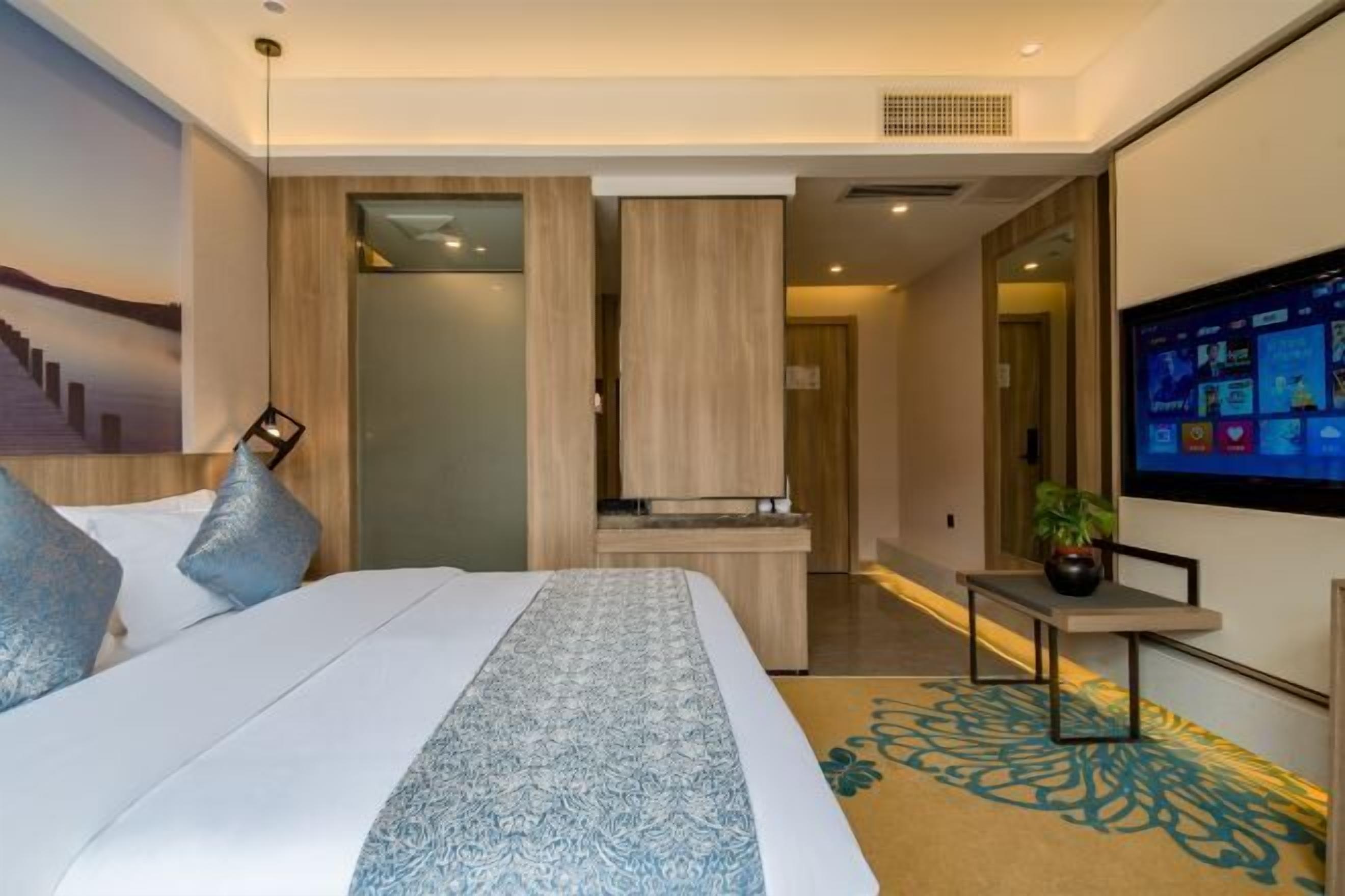 Une chambre d’hôtel moderne avec un grand lit, un téléviseur fixé au mur et une petite table agrémentée d’une plante.