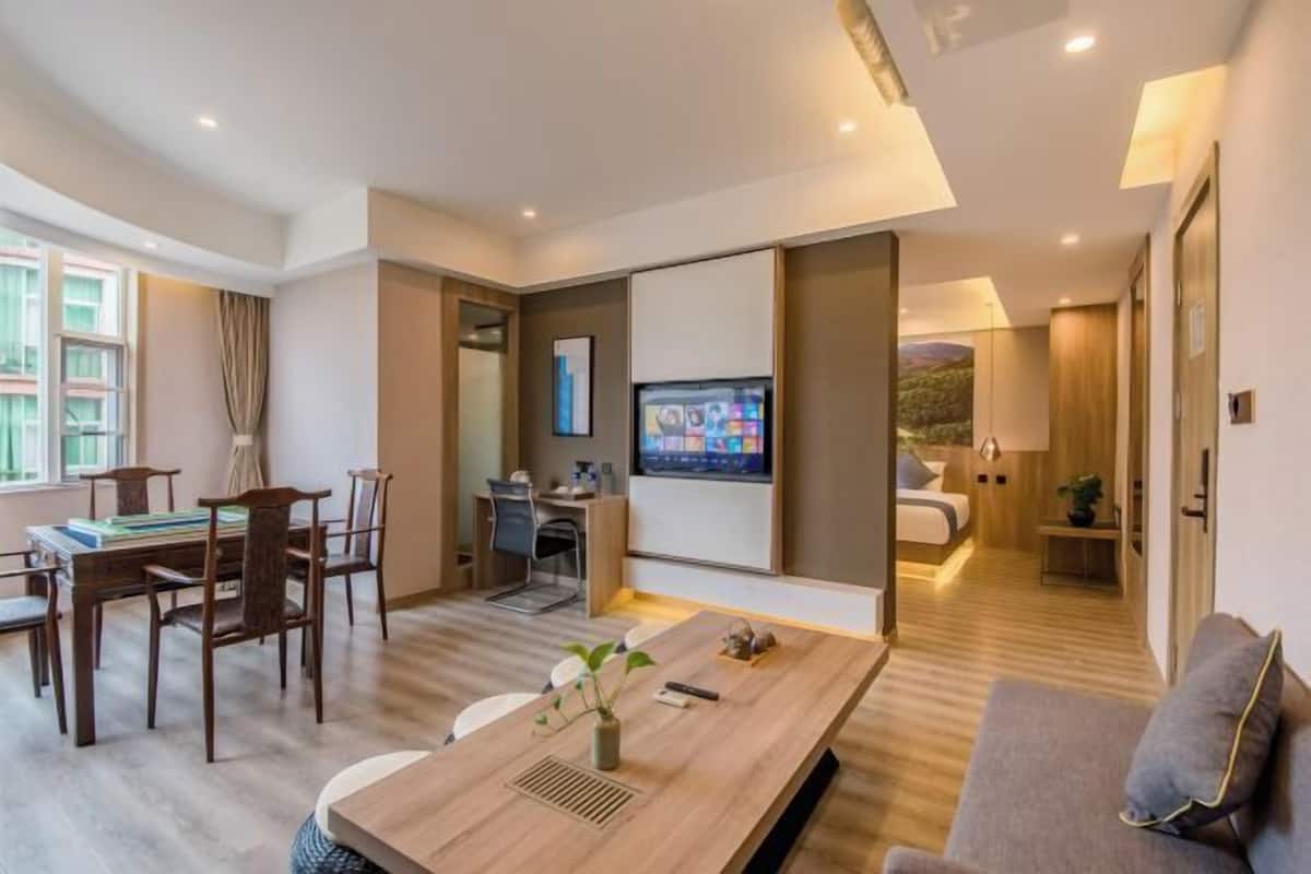 Una habitación de hotel moderna con zona de comedor, televisor, sofá y cama.