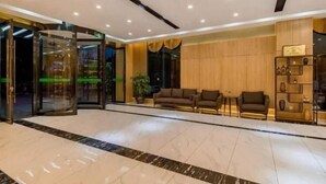 A lobby with a marble floor, a revolving door, and a seating area with sofas and a small table. - Manya Hotel (Xinping)