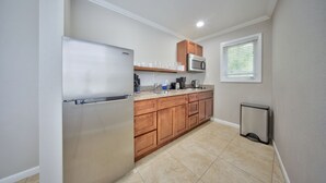 A kitchen with a stainless steel refrigerator, wooden cabinets, a microwave, and a window with blinds. - Surf and Sand Seaside (Pompano Beach)