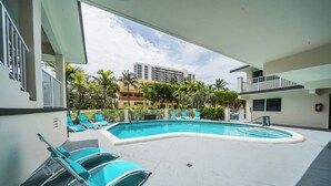 A swimming pool with lounge chairs, a building in the background, and a clear sky. - Surf and Sand Seaside (Pompano Beach)