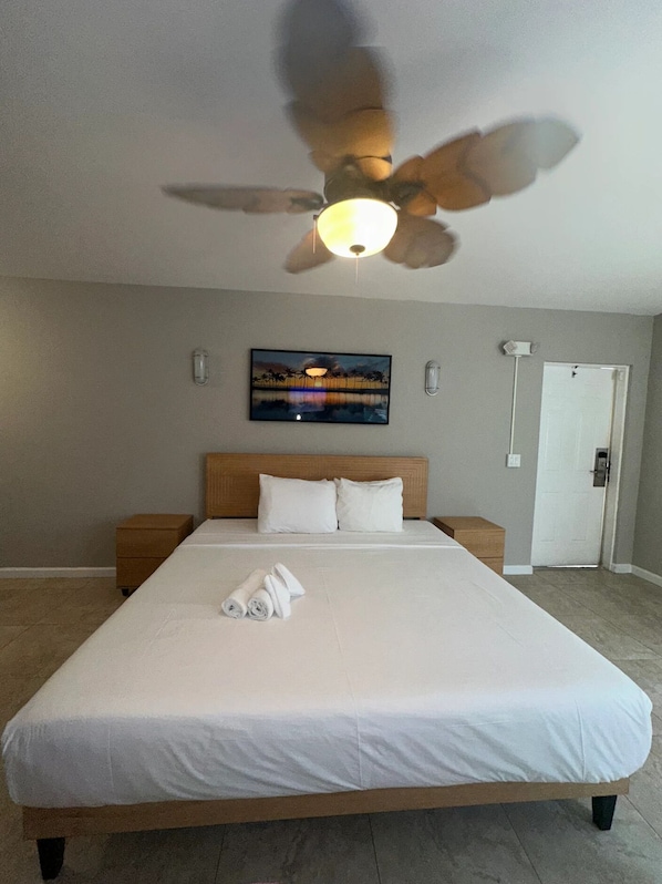 A hotel room with a large bed, a ceiling fan, a painting on the wall, and a door. - Surf and Sand Seaside (Pompano Beach)