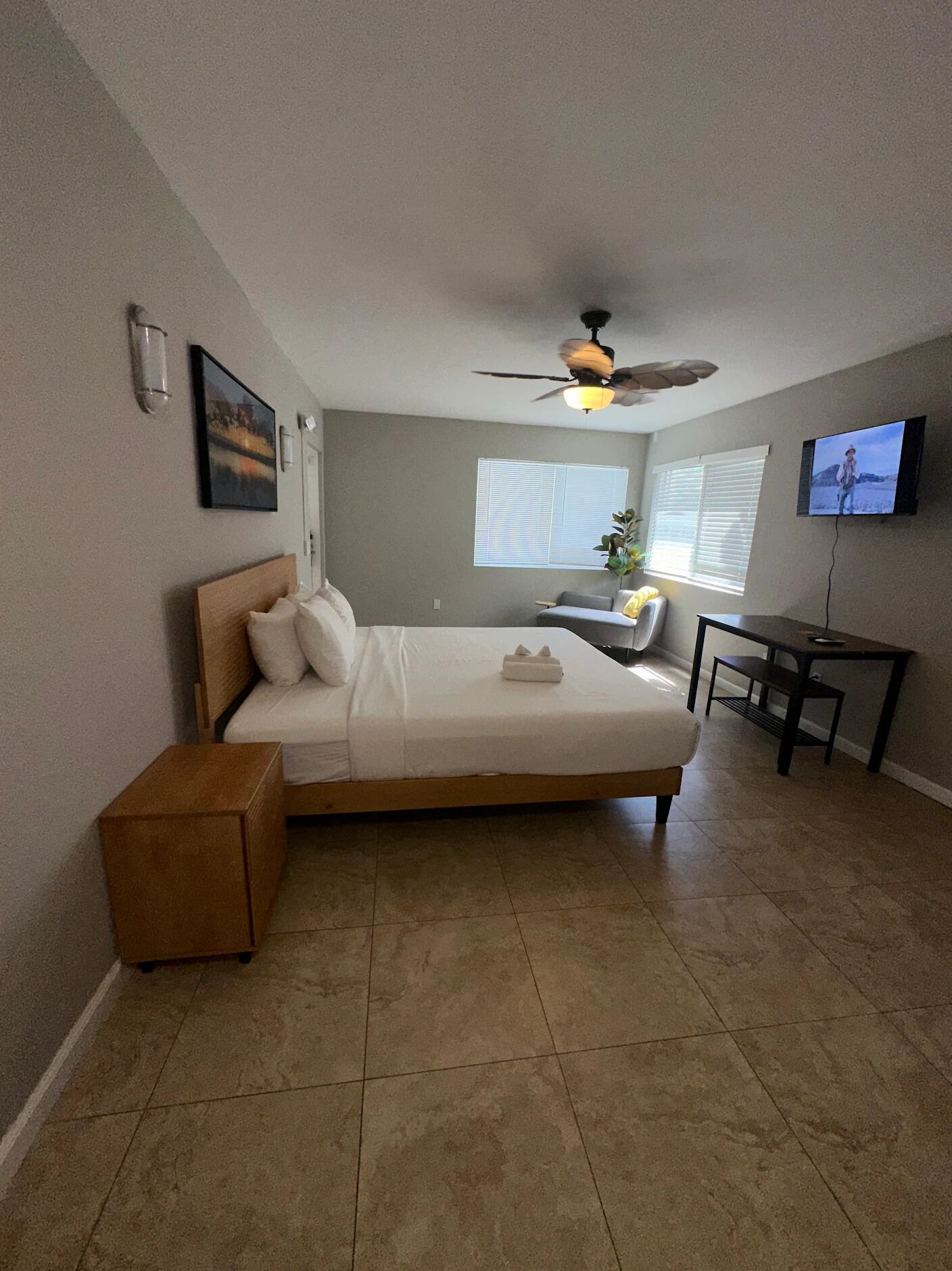A bedroom with a bed, a desk, a chair, a ceiling fan, and a TV.