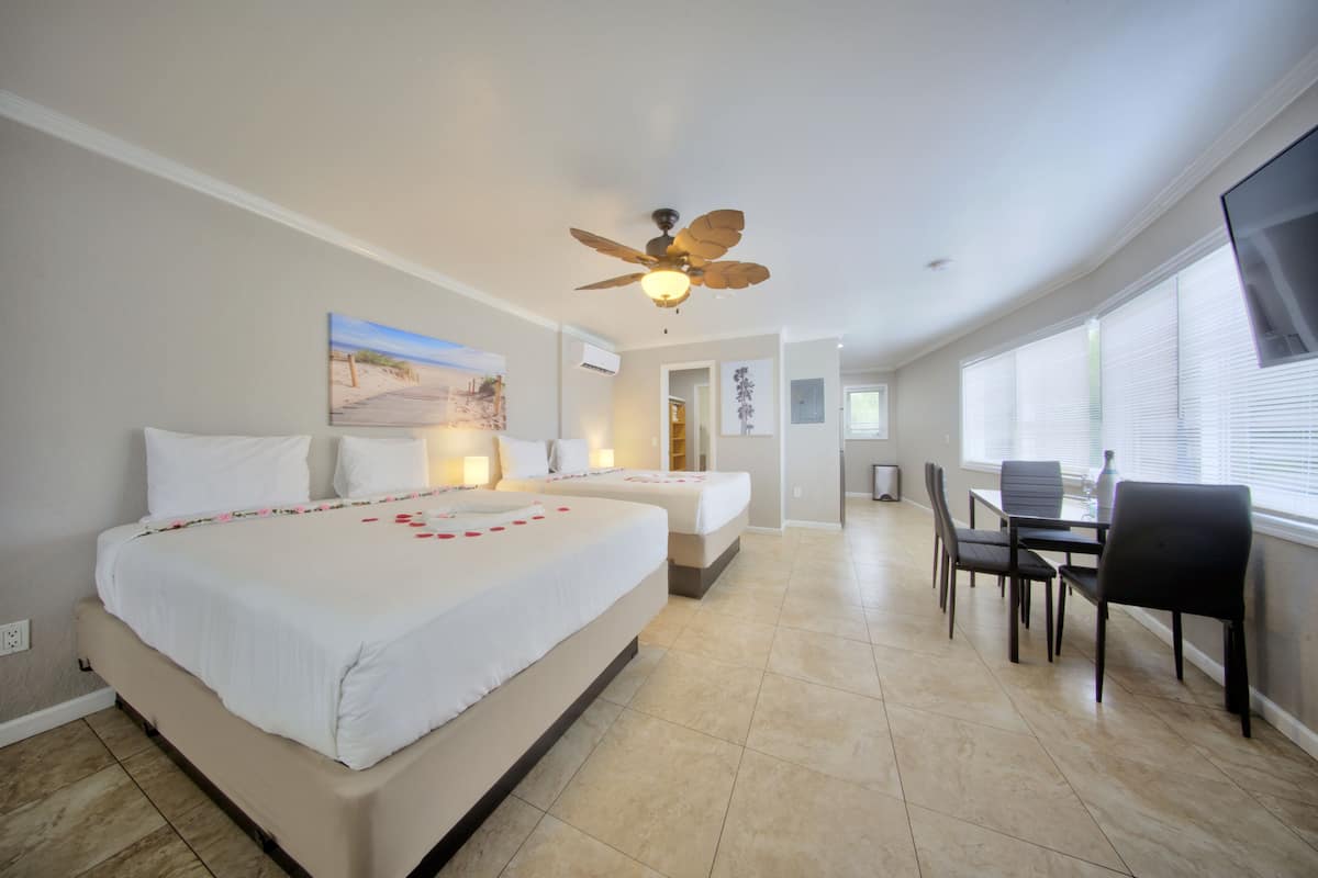 A hotel room with a large bed, a ceiling fan, a dining area with chairs and a table, and a TV mounted on the wall.