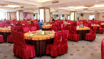 A banquet hall with round tables and red chairs, arranged in rows.