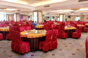 A banquet hall with round tables, red chairs, and a carpeted floor.