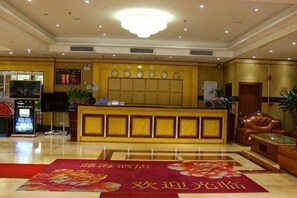 A hotel lobby with a reception desk, a red carpet, and a chandelier.