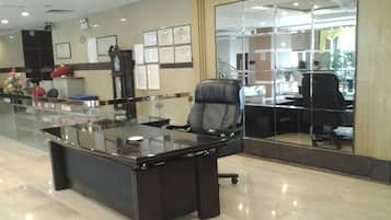 A modern office with a glass partition, a desk with a chair, and a large mirror reflecting the interior.