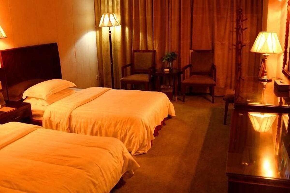 A hotel room with two beds, a desk, a chair, and a lamp.
