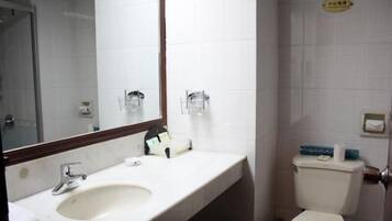 Un baño con lavamanos, espejo, inodoro y toallero.