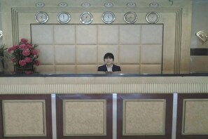 A reception desk with a clock, a potted plant, and a person seated behind it. - Foshan Tenghai Hotel (Foshan)