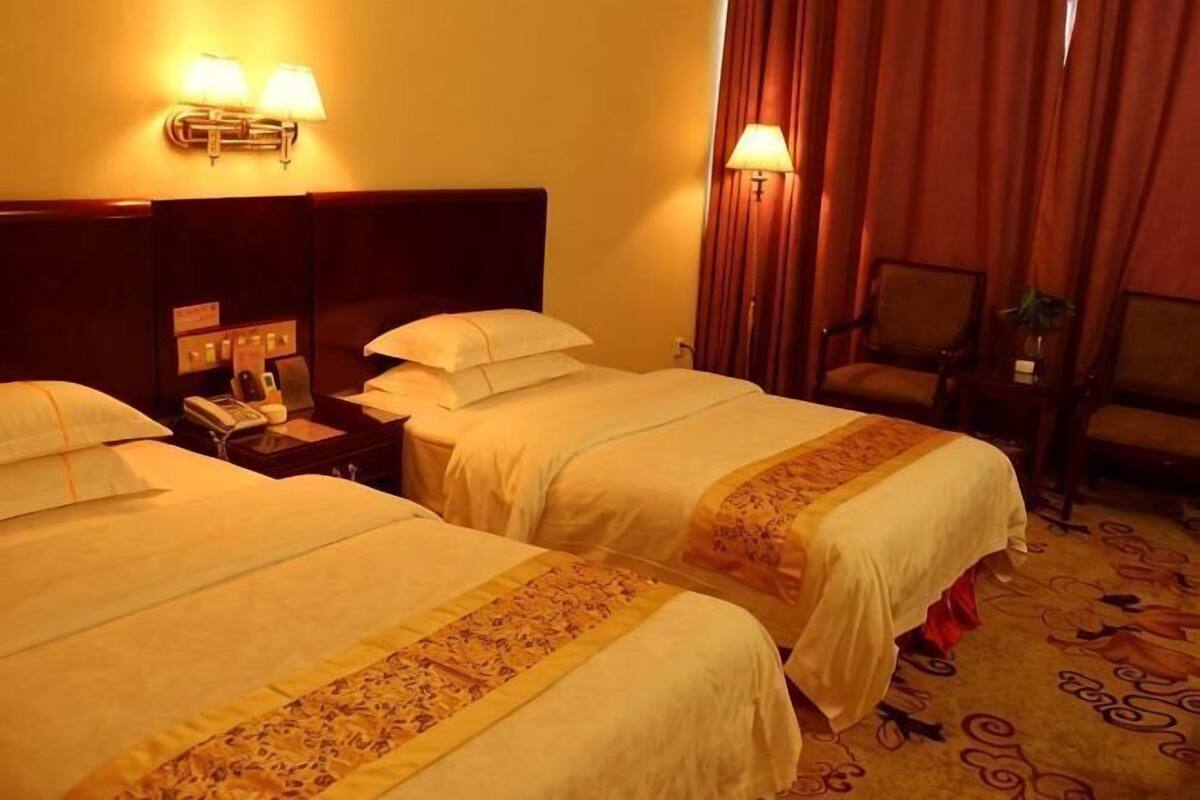 A hotel room with two beds, a nightstand with a phone, and a chair.