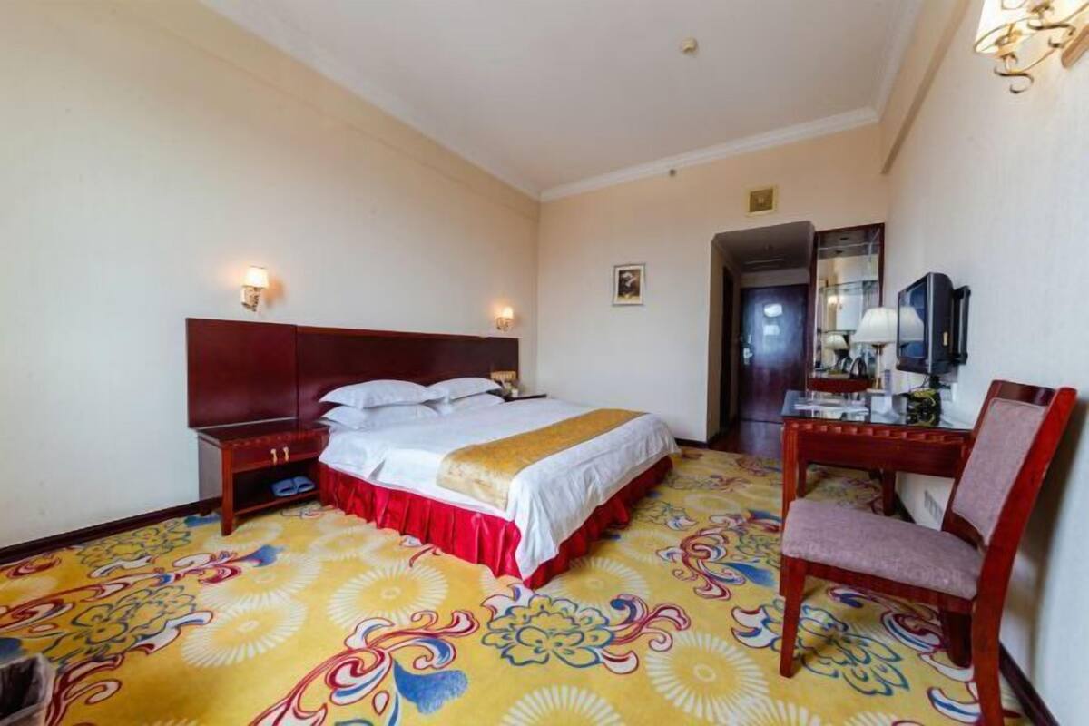 A hotel room with a bed, bedside table, chair, and a mirror.