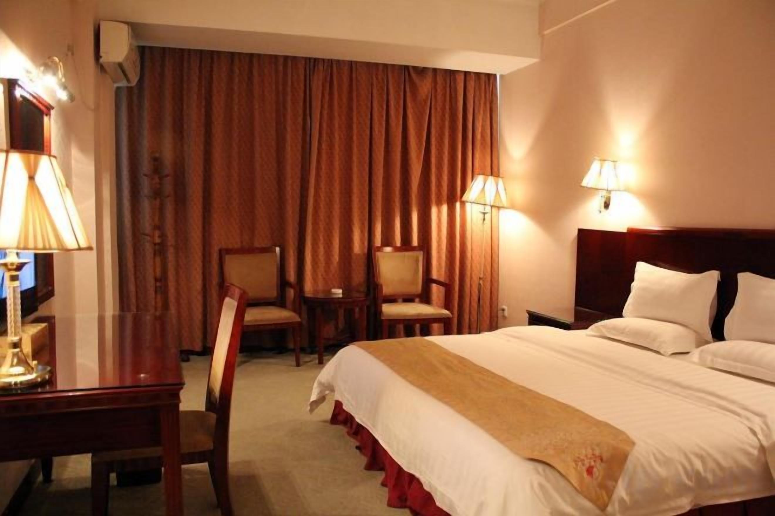 Habitación de hotel con cama, dos sillas, un escritorio y lámparas.