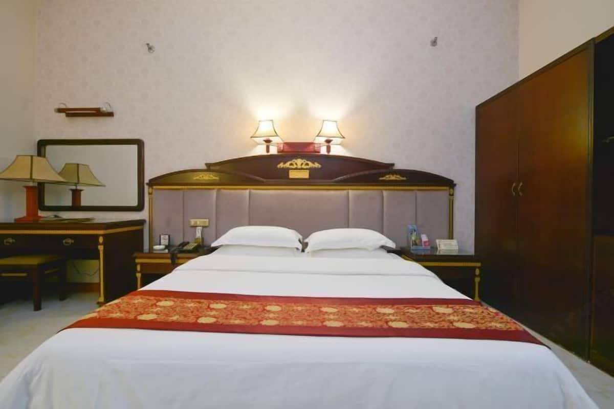 A hotel room with a large bed, two bedside lamps, a nightstand, a desk, a mirror, and a wardrobe.