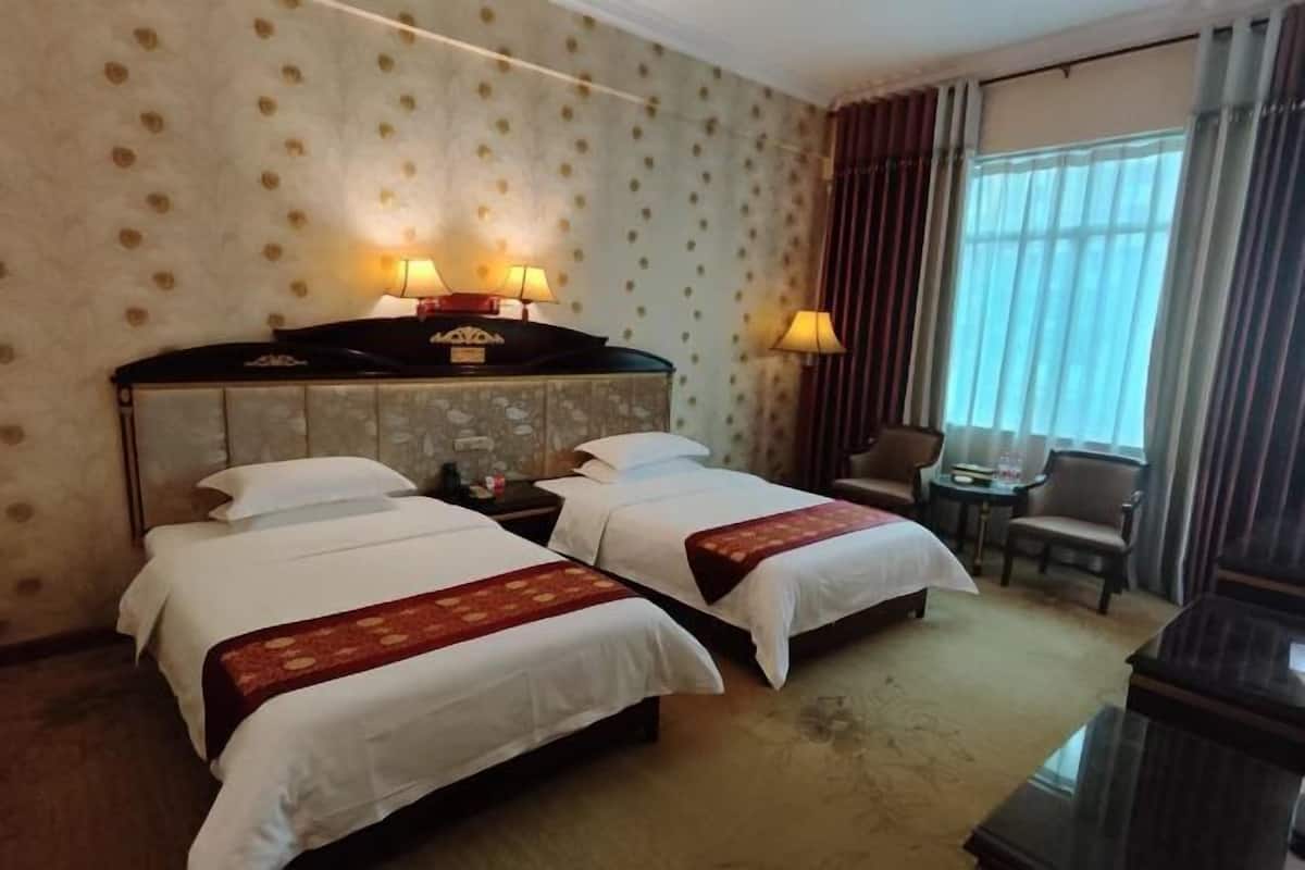 A hotel room with two beds, a nightstand, a desk, a chair, and a large window with curtains.