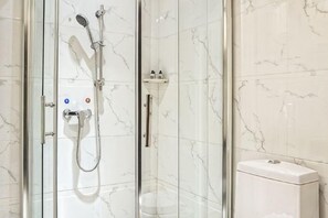A glass-enclosed shower with a handheld showerhead and a wall-mounted faucet. - Junmei International Hotel (Guigang)