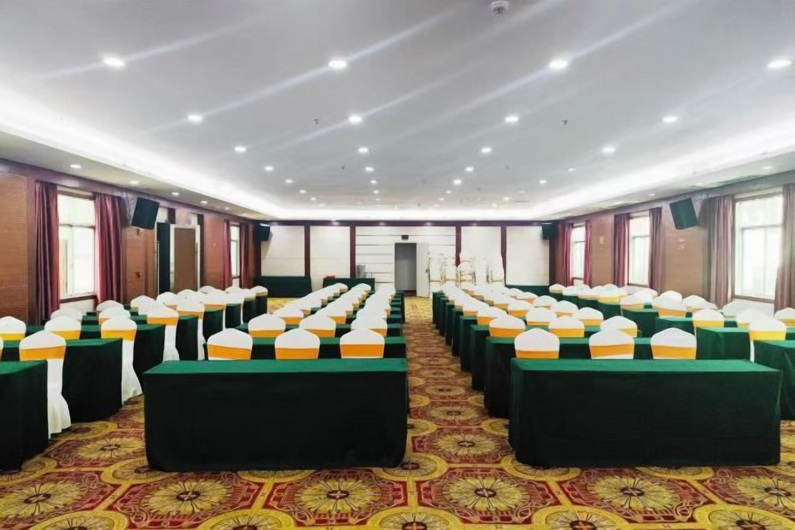 A conference room with rows of tables and chairs, a patterned carpet, and a ceiling with recessed lighting.