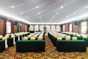 Un salón de conferencias con filas de mesas y sillas, una alfombra estampada e iluminación empotrada en el techo.