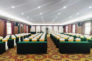 A conference room with rows of tables and chairs, a patterned carpet, and a ceiling with recessed lighting.