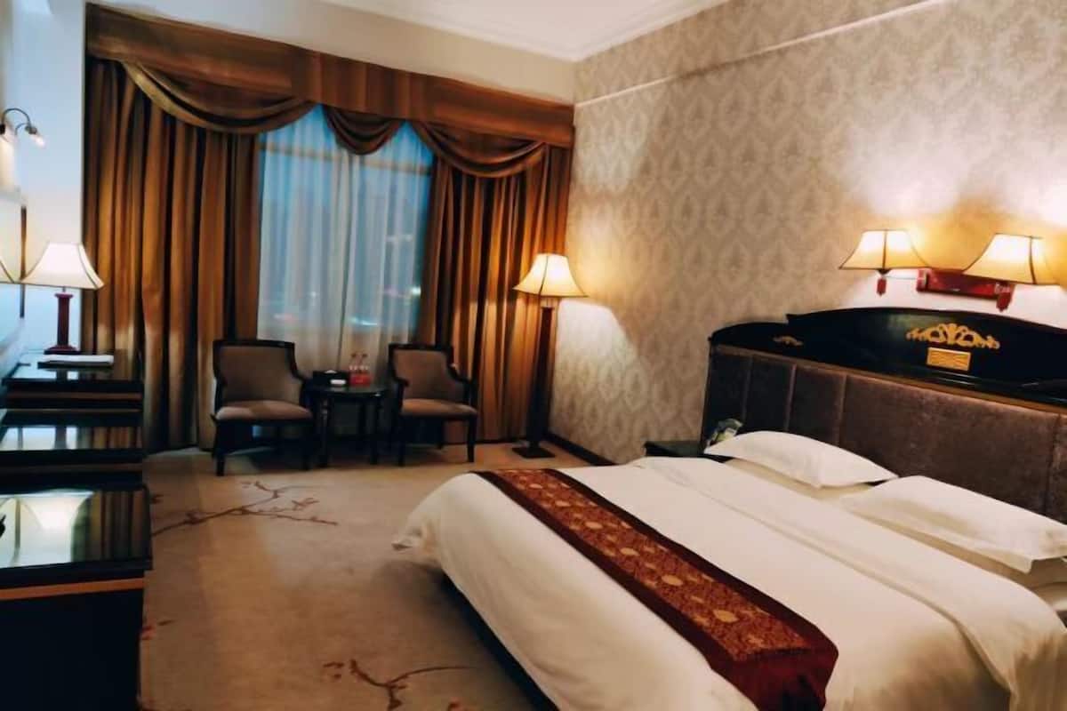 A hotel room with a bed, two chairs, a desk, a piano, and two lamps.