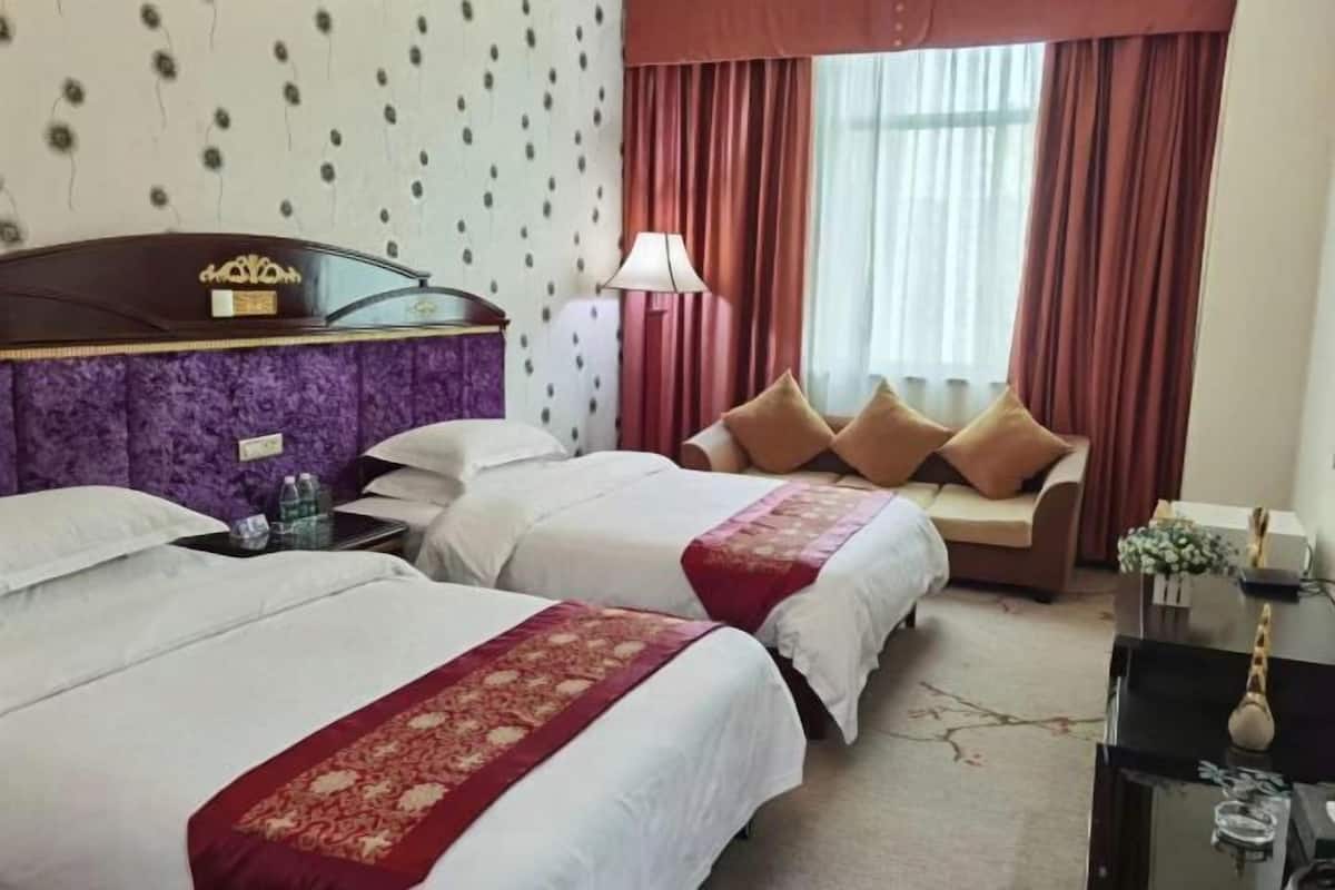 A hotel room with two beds, a sofa, a desk, and a window with curtains.