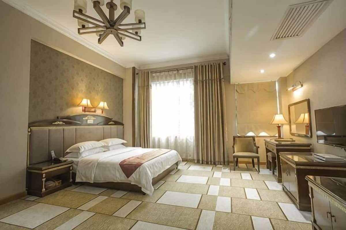 A hotel room with a bed, bedside tables, a desk, a chair, a TV, and a window with curtains.