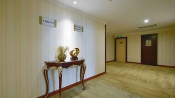 A hotel hallway with a marble floor, a reception desk with a vase and a sculpture, and directional signs.
