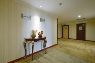 Pasillo de hotel con suelo de mármol, una recepción con un jarrón y una escultura, y señalización.