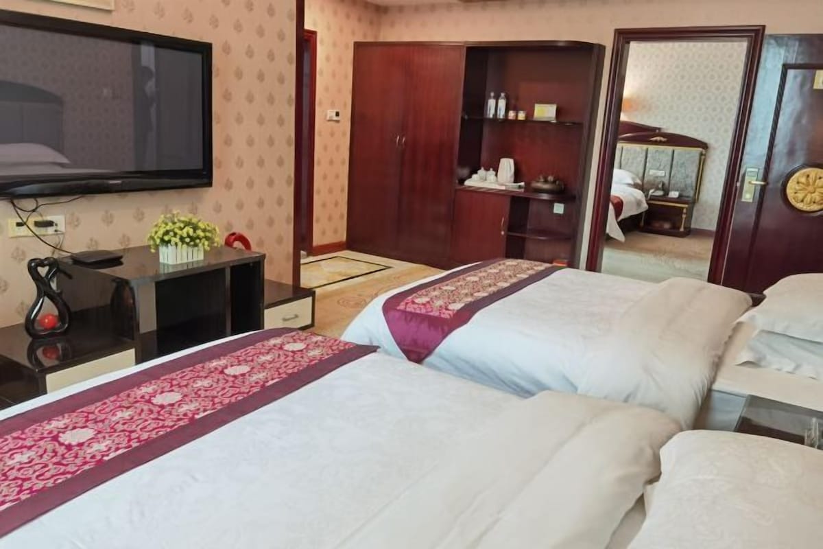 Une chambre d’hôtel avec deux lits, une télévision, une armoire et un petit bureau agrémenté d’une plante.