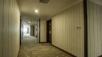 Un pasillo de hotel con alfombra estampada, puertas y un interruptor de luz en la pared.