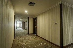 Corredor de hotel com carpete estampado, portas e interruptor de luz na parede.