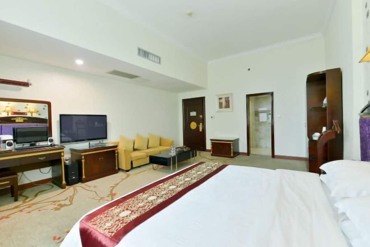 A hotel room with a bed, a desk with a computer, a television, a sofa, and a carpeted floor.