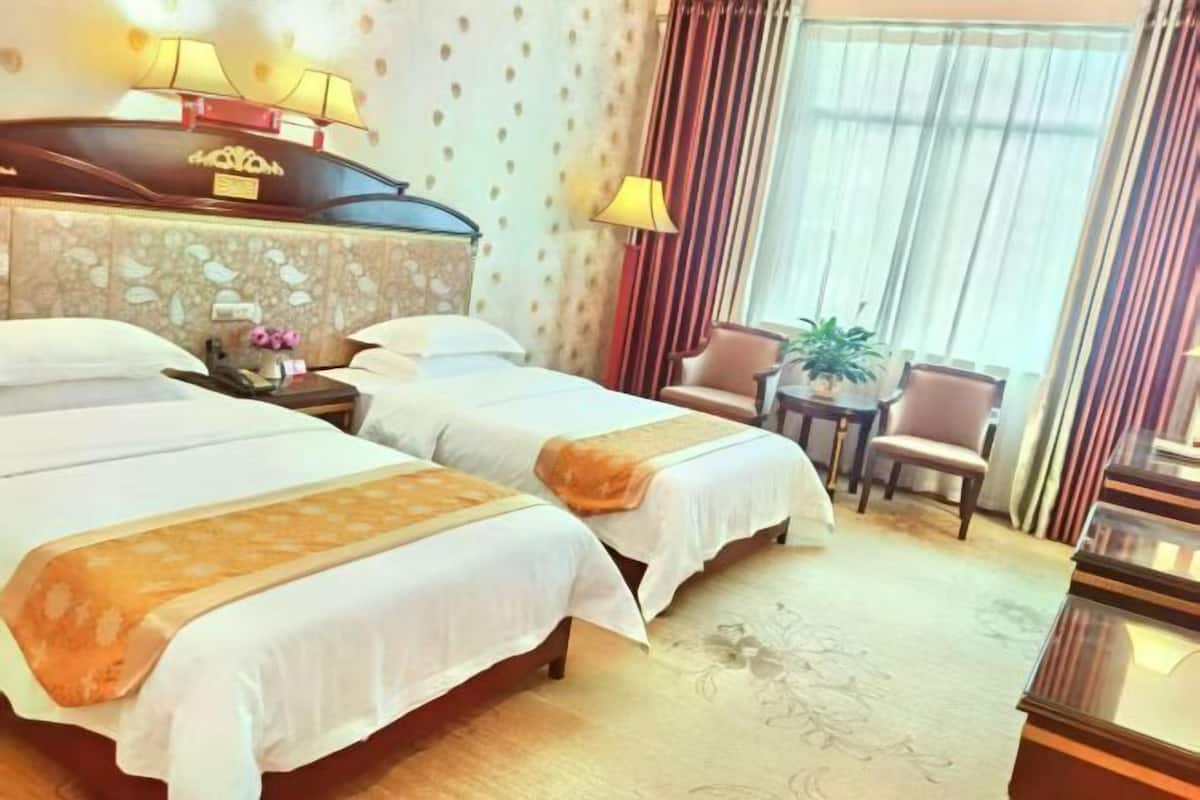 A hotel room with two beds, a nightstand, a chair, a small table, and a lamp.