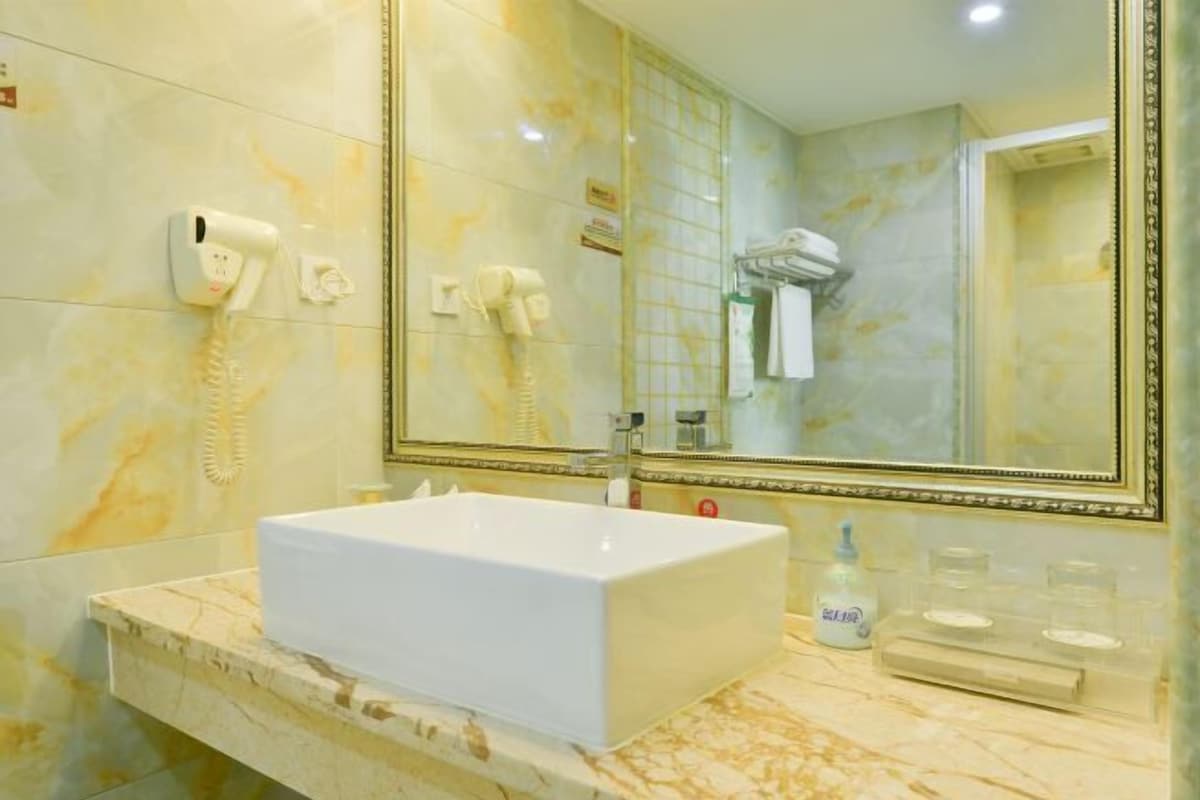 Une salle de bain avec un lavabo blanc, un grand miroir et un sèche-cheveux fixé au mur.
