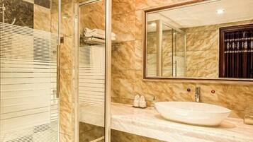 A bathroom with a glass shower enclosure, a marble vanity, and a large mirror.
