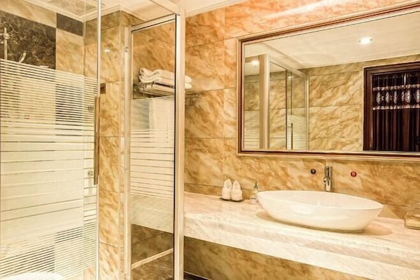 Une salle de bain dotée d’une douche à parois de verre, d’un meuble-lavabo en marbre et d’un grand miroir.