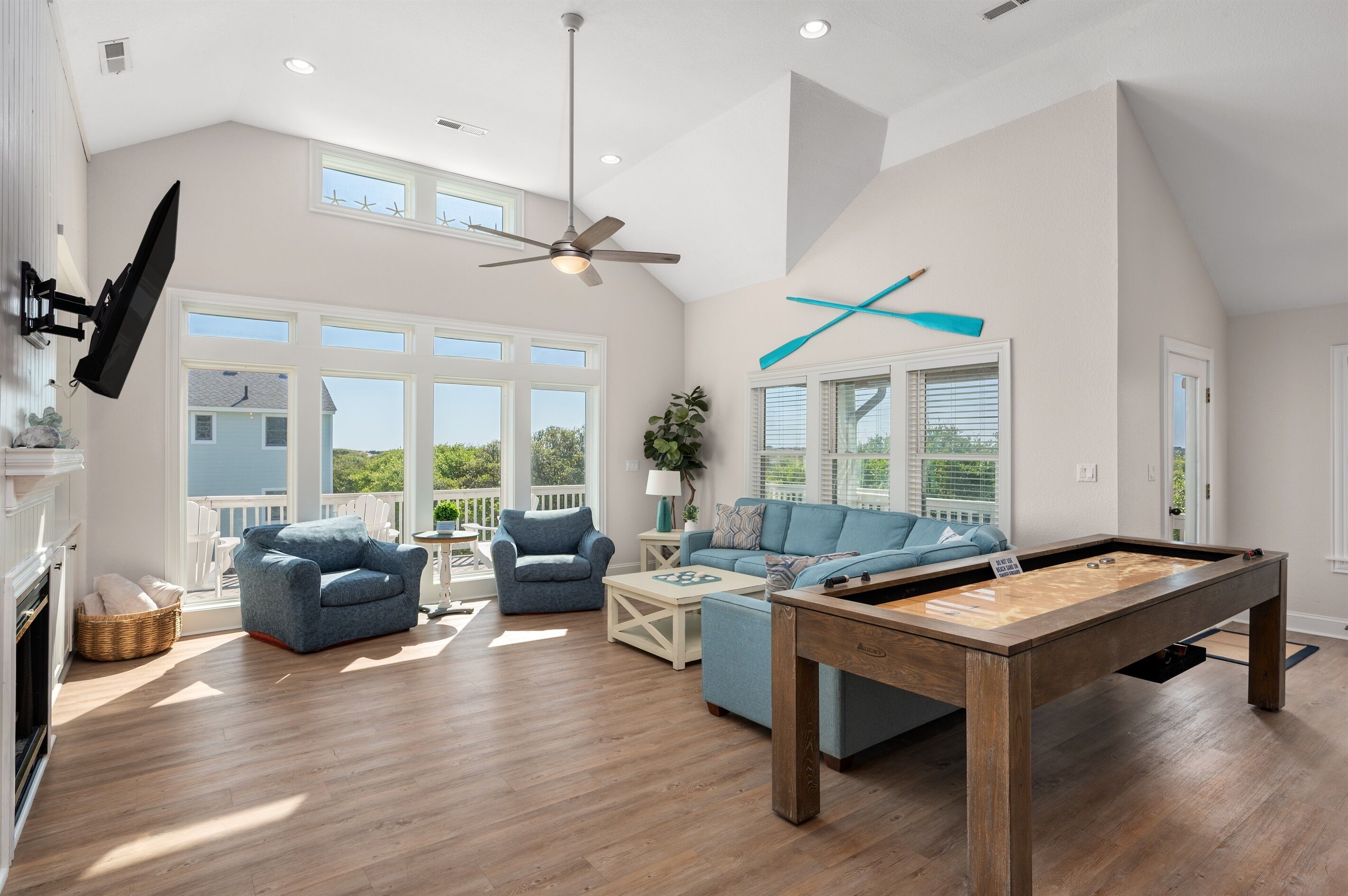 A spacious living room with a pool table, two blue armchairs, a sofa, and a ceiling fan.