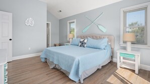 Une chambre à coucher comprenant un lit, un ventilateur de plafond, une fenêtre avec des stores et un élément décoratif fixé au mur.