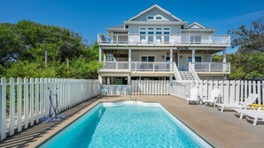 Une maison à deux étages avec une piscine, une clôture blanche en bois et un espace salon extérieur.