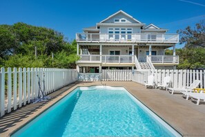 A two-story house with a swimming pool, white picket fence, and outdoor seating. - Sea Haven- Heated Salt Water Pool | Sleeps 16 | Dogs OK |500ft to beach |Hot Tub (Corolla)