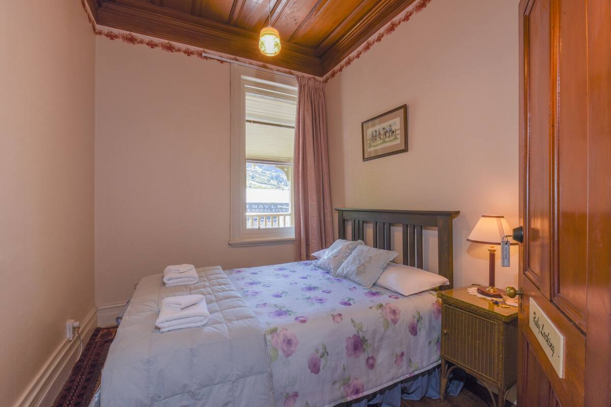 A neatly made bed with a floral bedspread, a bedside table with a lamp, and a window with curtains.