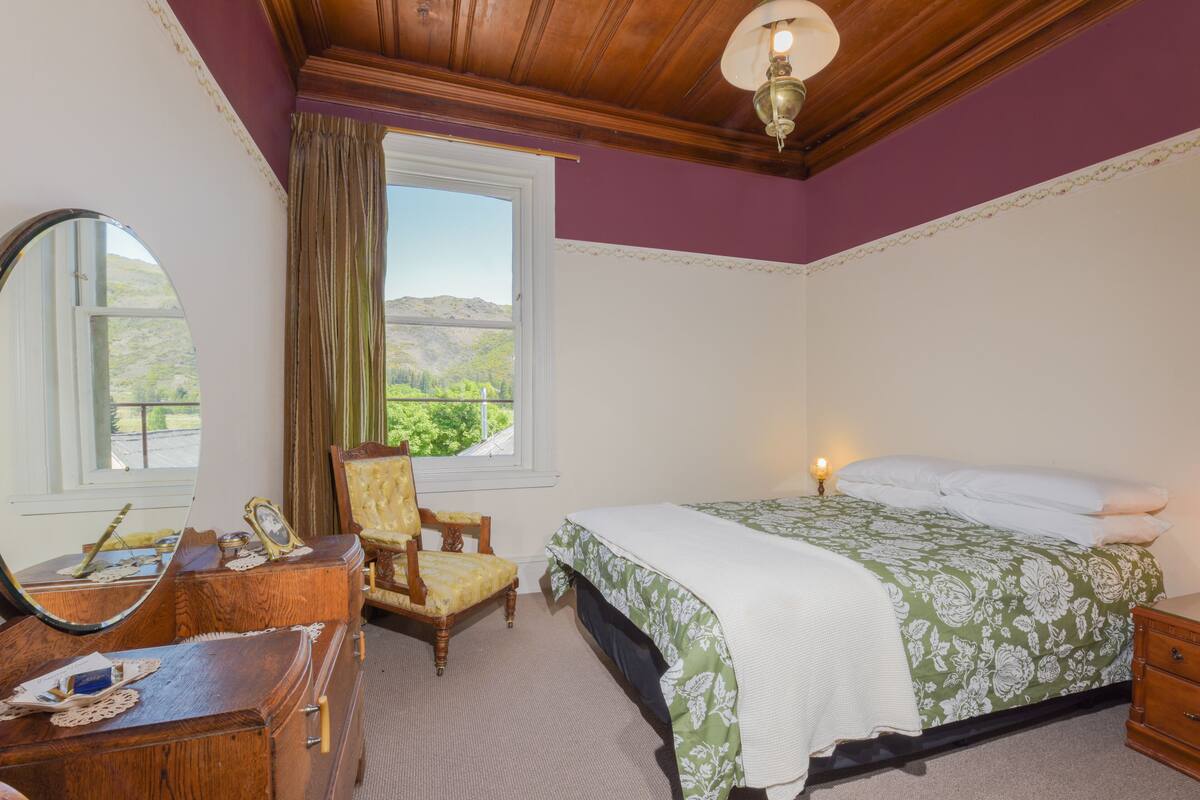 A bedroom with a bed, a chair, a dresser, and a window with a view of greenery.