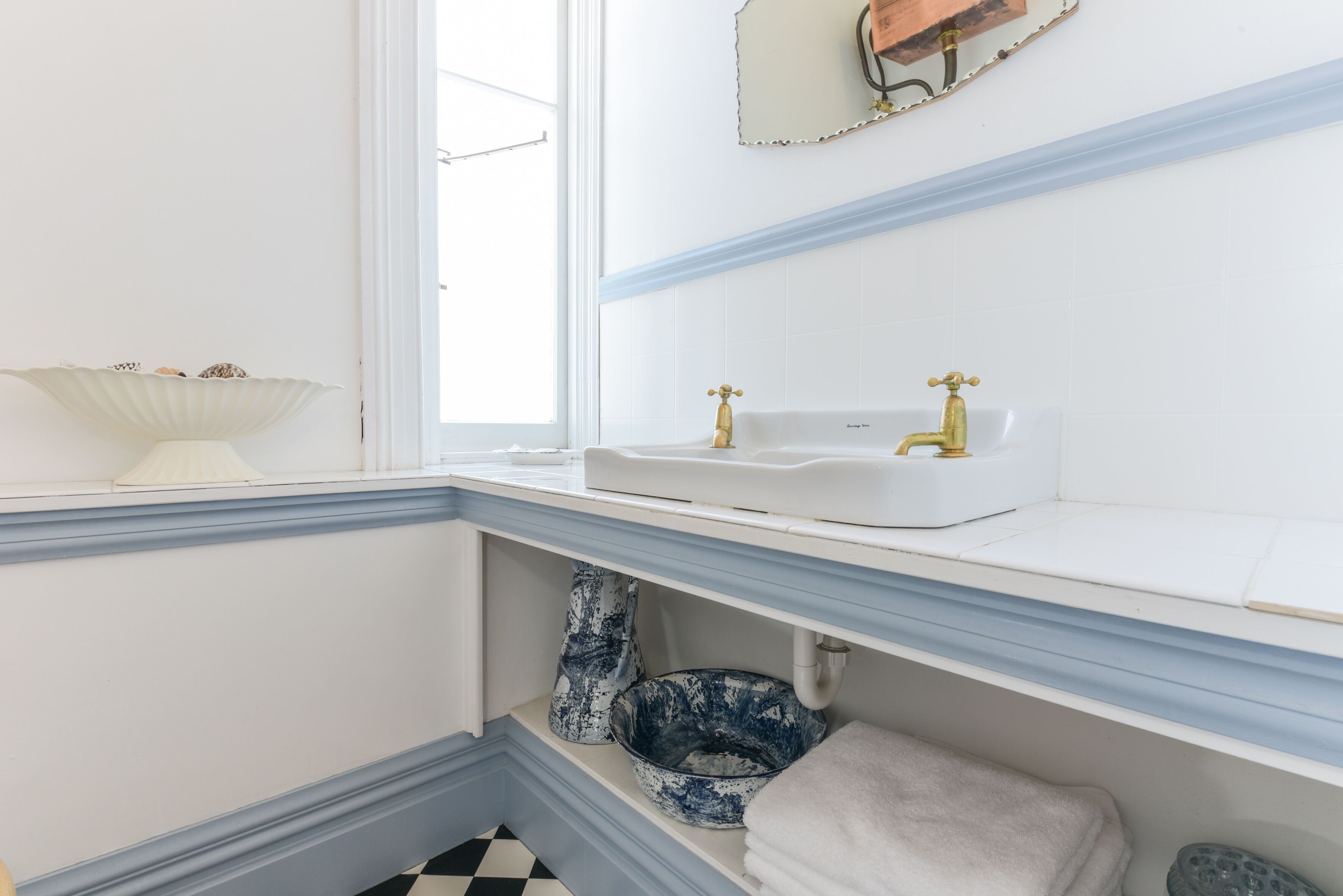 A bathroom with a white sink, gold faucets, and a blue and white vase.